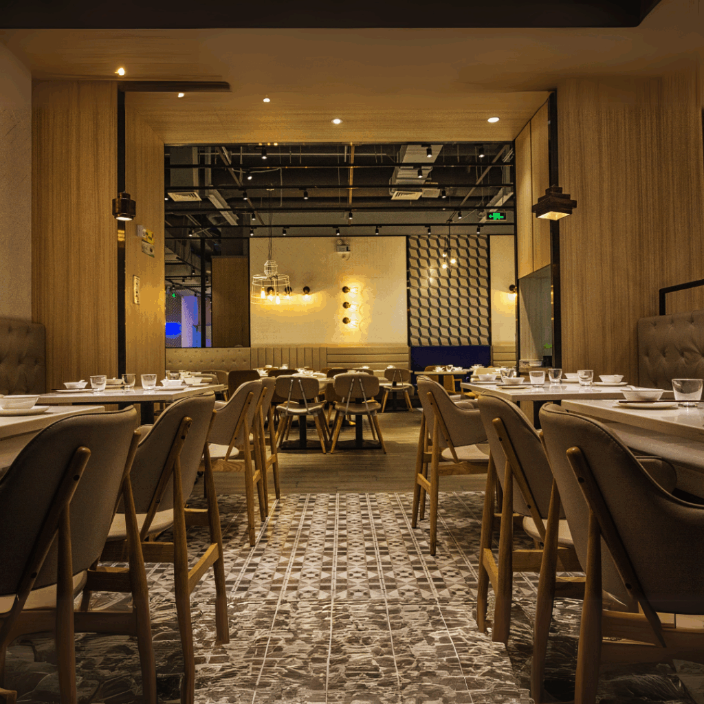 Modern eingerichtetes Restaurant mit Holzverkleidung, gepolsterten Stühlen, gedeckten Tischen und stilvollen Deckenleuchten in warmem Licht.